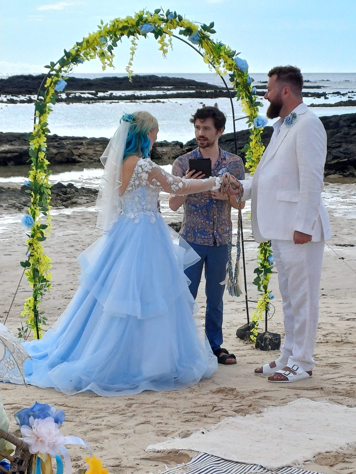 Beach ceremony with couple standing under a yellow and blue floral arch