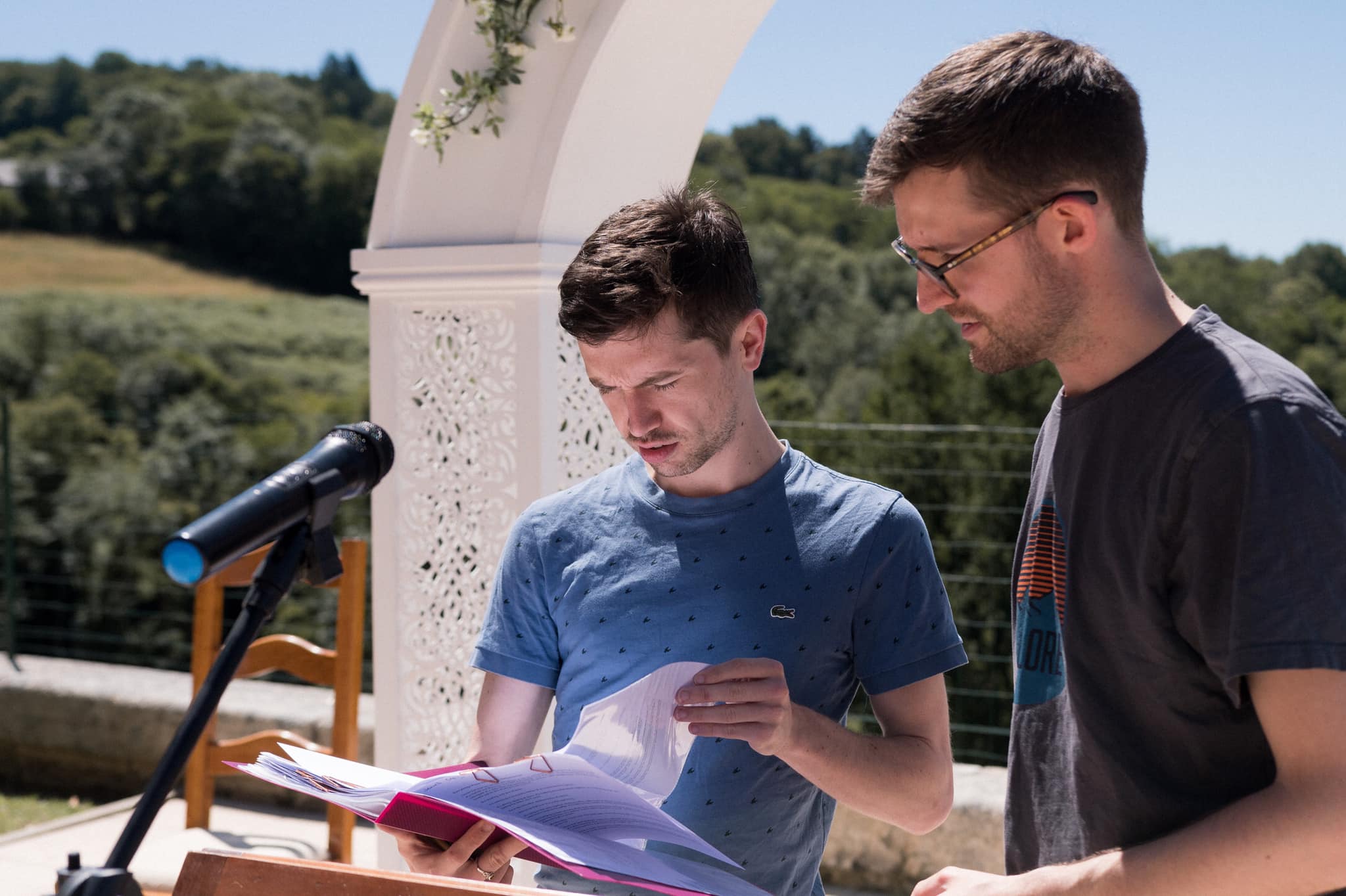 Jack speaking with a bride and groom under a white stone arch, in black and white